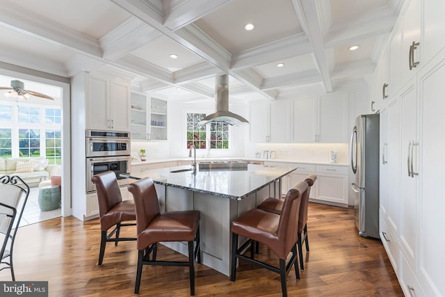 kitchen featuring appliances with stainless steel finishes, beam ceiling, a breakfast bar area, and island range hood