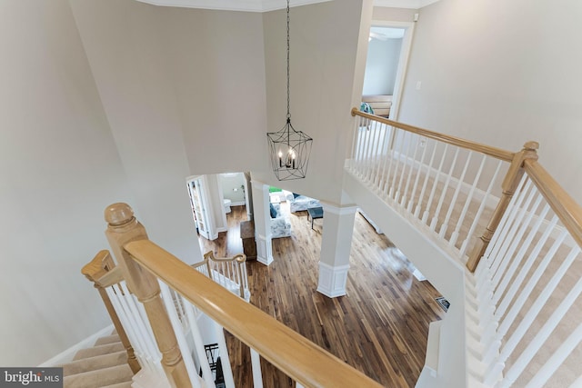 staircase with wood finished floors, a high ceiling, a notable chandelier, and baseboards