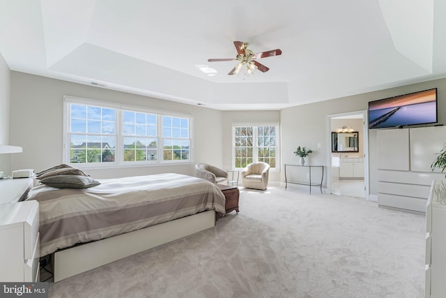 carpeted bedroom with a ceiling fan, visible vents, a raised ceiling, and ensuite bath