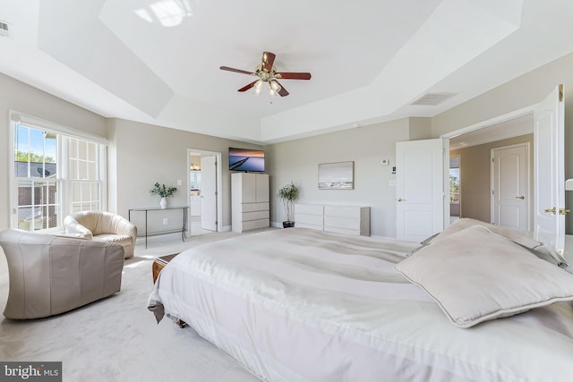 carpeted bedroom featuring visible vents, a ceiling fan, ensuite bathroom, and a tray ceiling