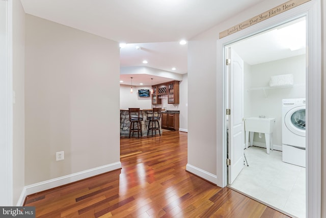 corridor with recessed lighting, a sink, washer / dryer, baseboards, and wood finished floors