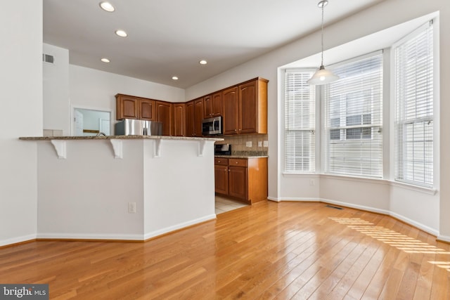kitchen featuring light wood-style floors, appliances with stainless steel finishes, a breakfast bar, and stone countertops