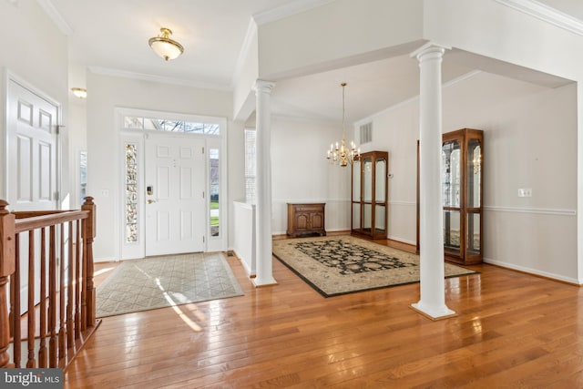 foyer with baseboards, decorative columns, a chandelier, crown molding, and hardwood / wood-style floors