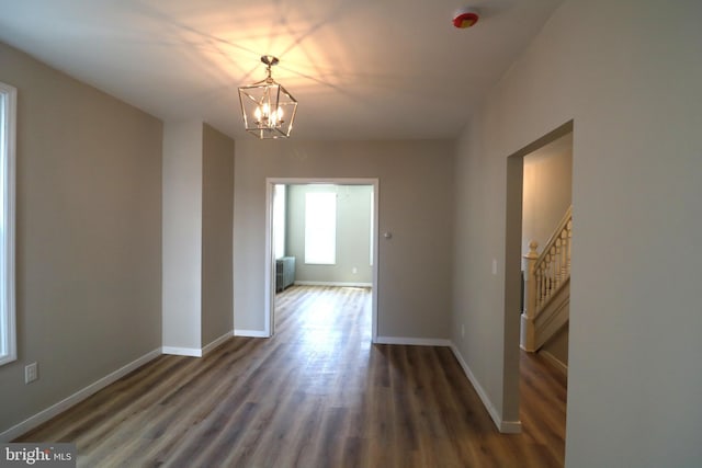 unfurnished dining area with baseboards, stairs, wood finished floors, and an inviting chandelier