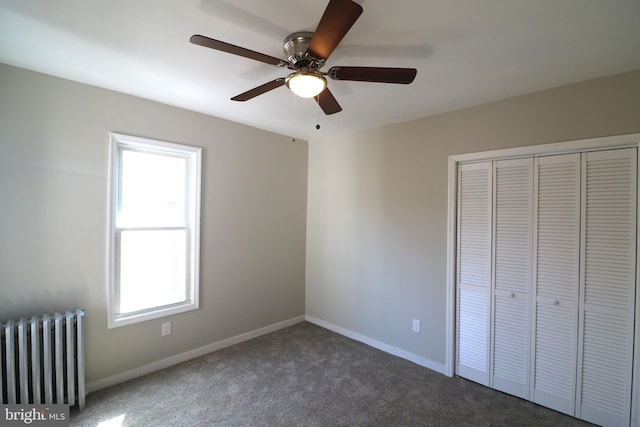 unfurnished bedroom featuring a closet, radiator heating unit, ceiling fan, baseboards, and dark carpet
