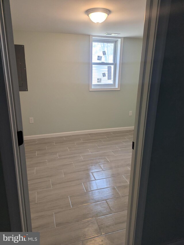 empty room with baseboards, visible vents, wood finished floors, and electric panel