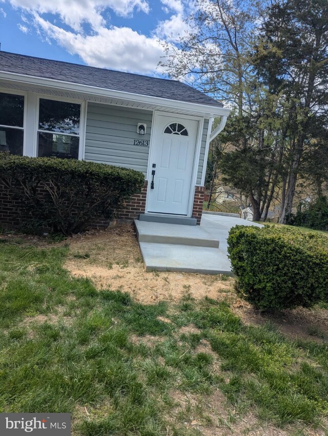 entrance to property featuring brick siding and roof with shingles