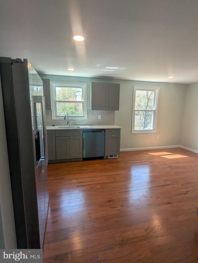 kitchen featuring stainless steel dishwasher, a healthy amount of sunlight, gray cabinetry, and hardwood / wood-style floors