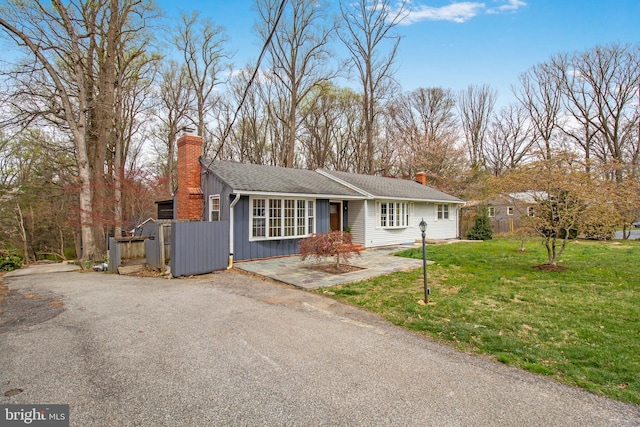 ranch-style home with driveway, board and batten siding, a front yard, and a chimney