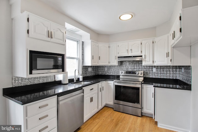 kitchen with white cabinets, dark countertops, appliances with stainless steel finishes, a sink, and under cabinet range hood