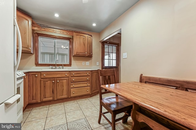 kitchen featuring light tile patterned floors, white appliances, brown cabinetry, light countertops, and a sink