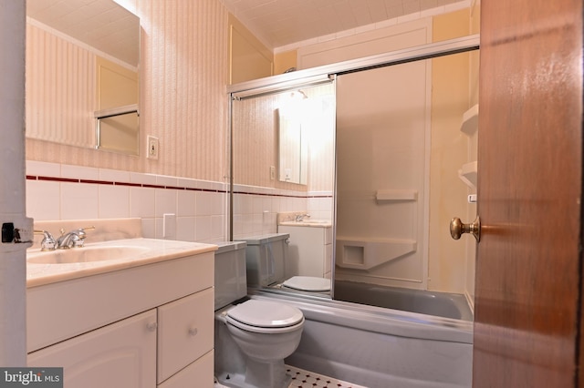 bathroom with tile walls, toilet, vanity, and shower / bath combination with glass door