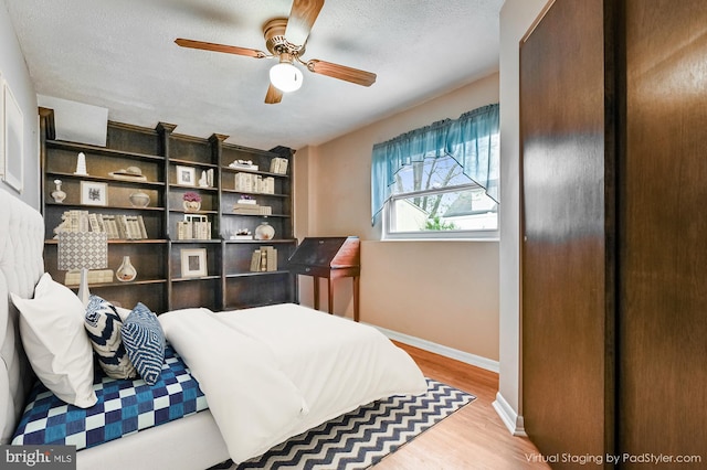 bedroom featuring wood finished floors, baseboards, a textured ceiling, and ceiling fan