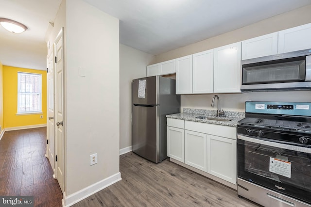 kitchen featuring white cabinetry, wood finished floors, a sink, and stainless steel appliances