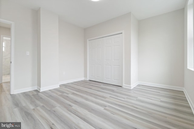unfurnished bedroom with a closet, light wood-style flooring, and baseboards