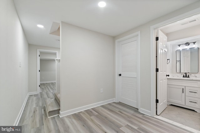 hallway with light wood-style floors, recessed lighting, a sink, and visible vents
