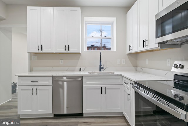 kitchen featuring stainless steel appliances, light stone counters, white cabinetry, and a sink