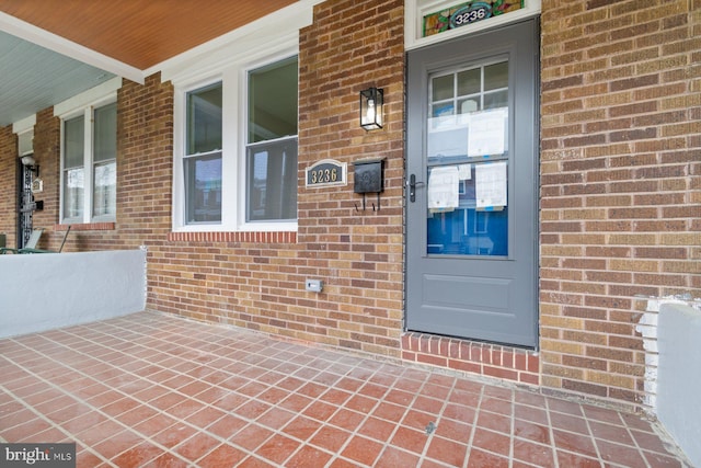 doorway to property featuring covered porch and brick siding