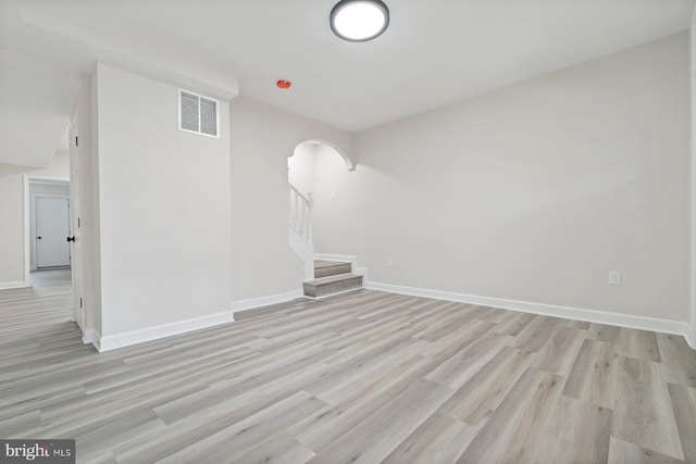 spare room featuring visible vents, arched walkways, light wood-style flooring, and stairway