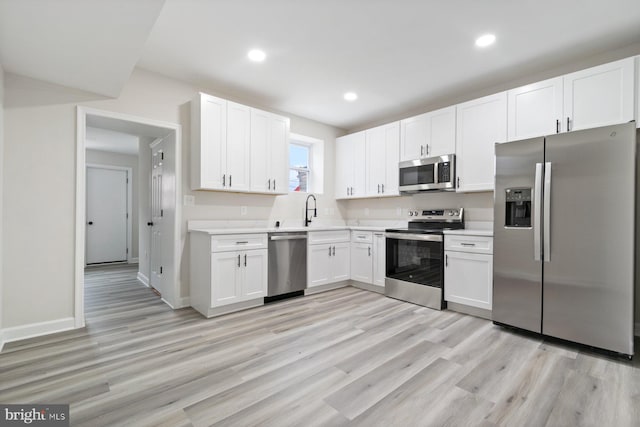 kitchen with a sink, light wood finished floors, appliances with stainless steel finishes, and white cabinets