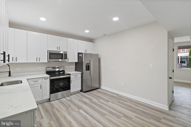 kitchen with light wood-style floors, a sink, appliances with stainless steel finishes, and light stone countertops