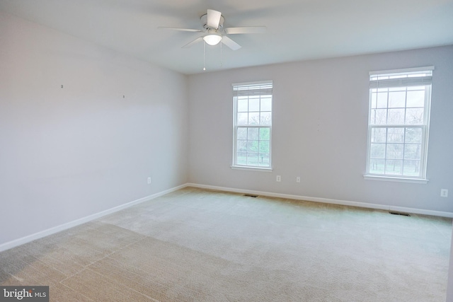 empty room featuring light carpet, visible vents, baseboards, and ceiling fan