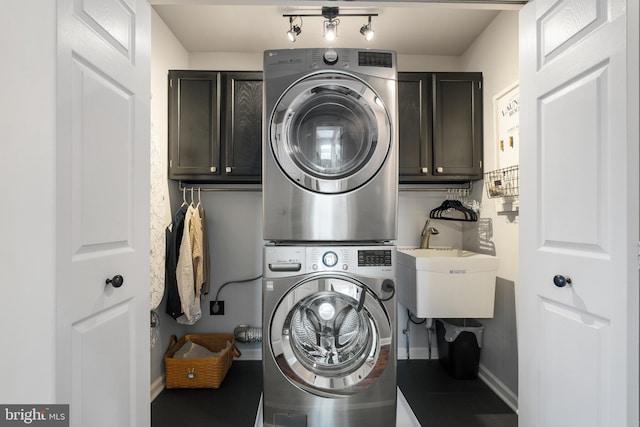 laundry room with baseboards, rail lighting, stacked washer / drying machine, cabinet space, and a sink