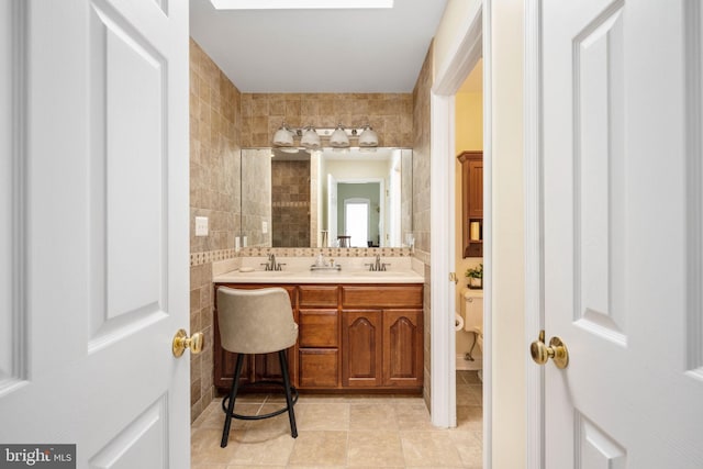 full bath featuring double vanity, a sink, toilet, and tile walls