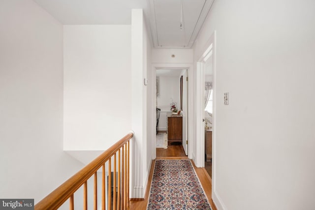 hall featuring attic access, baseboards, and light wood finished floors