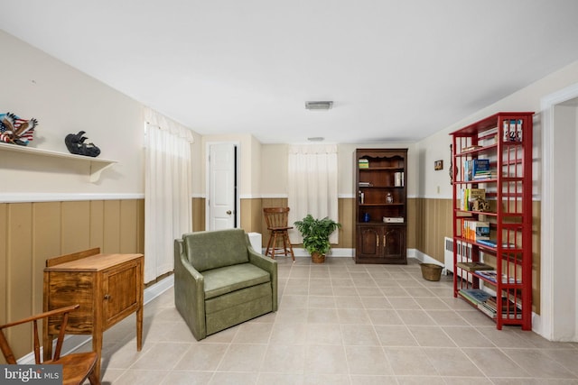 living area with a wainscoted wall, light tile patterned flooring, wooden walls, and visible vents