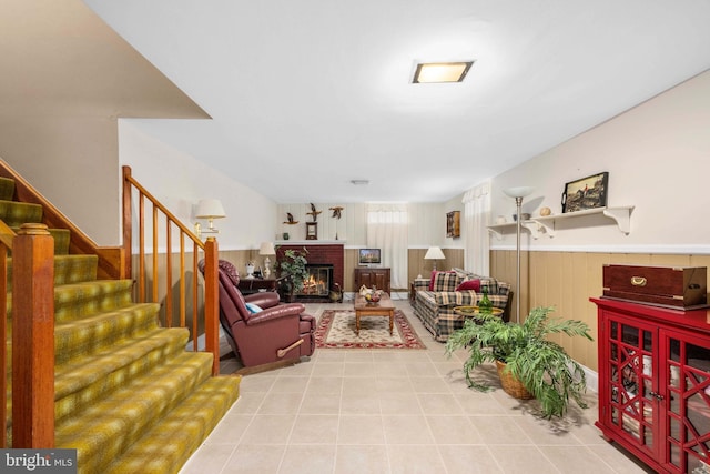 living room featuring a wainscoted wall, wood walls, a fireplace, stairway, and tile patterned flooring