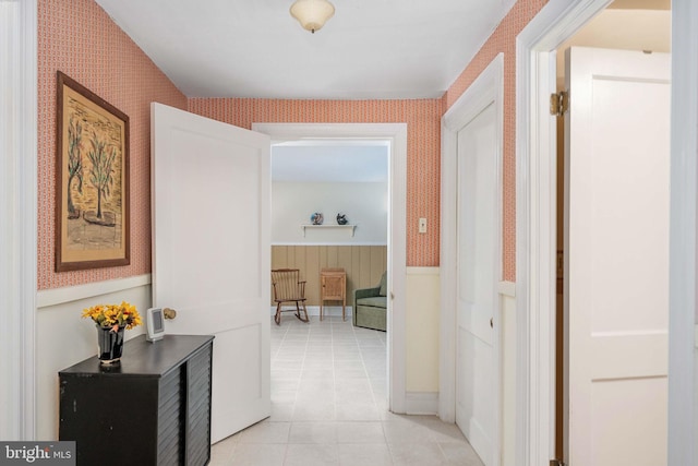 corridor with wallpapered walls, light tile patterned floors, and wainscoting