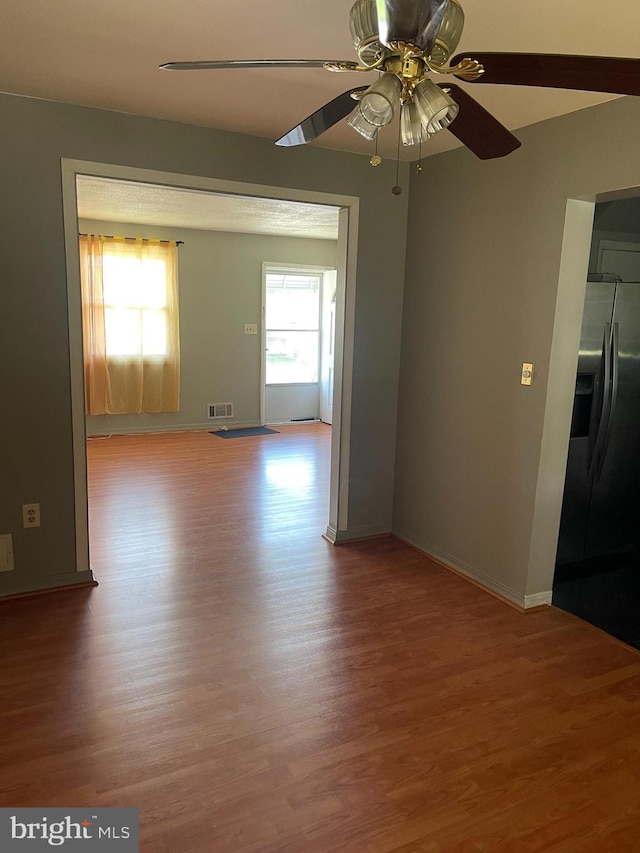 empty room with baseboards, ceiling fan, wood finished floors, and visible vents