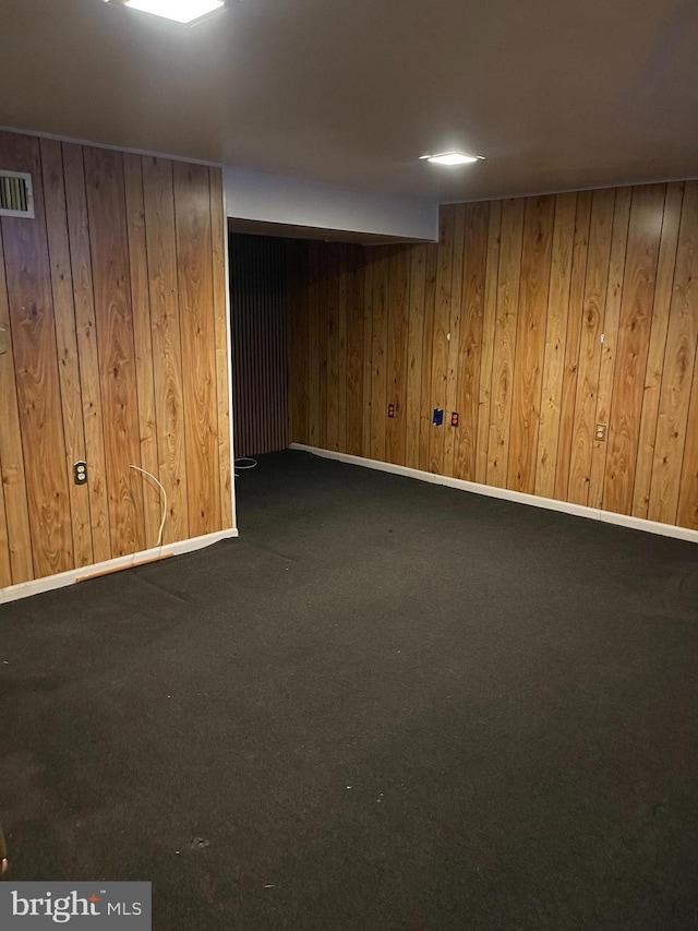 finished below grade area featuring carpet floors, wood walls, baseboards, and visible vents