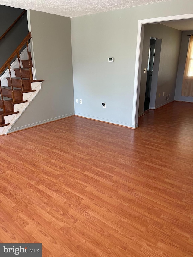 unfurnished living room featuring baseboards, light wood finished floors, and stairway