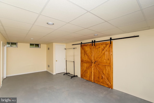 finished below grade area with a barn door, a paneled ceiling, and baseboards