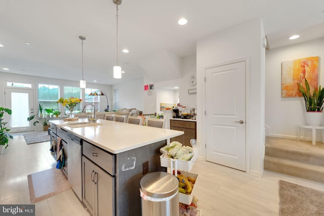 kitchen featuring a sink, open floor plan, light countertops, stainless steel dishwasher, and pendant lighting