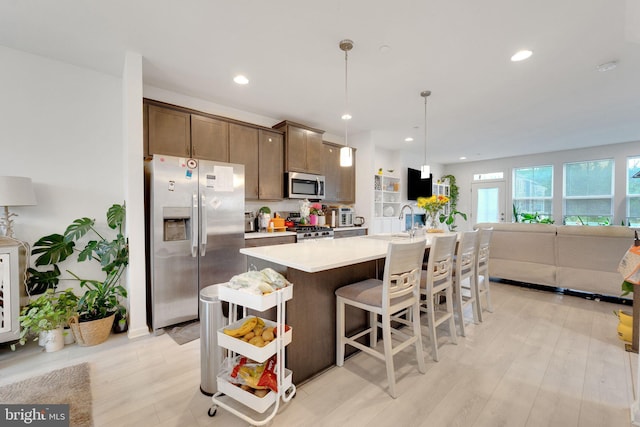 kitchen featuring stainless steel appliances, light countertops, a kitchen island with sink, recessed lighting, and a kitchen bar