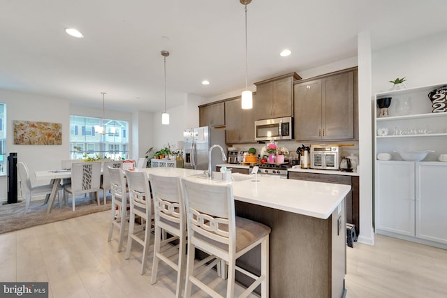 kitchen with stainless steel appliances, a sink, light countertops, a breakfast bar area, and light wood-type flooring