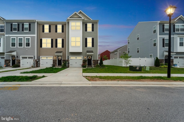 multi unit property with an attached garage, driveway, stone siding, and fence