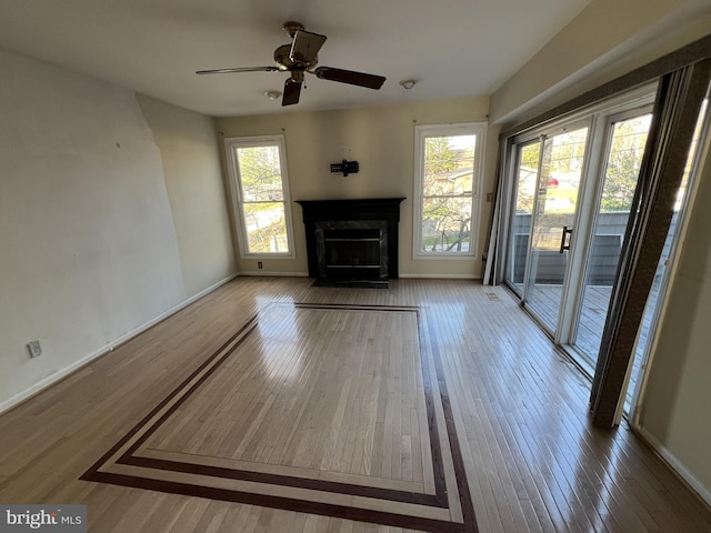 unfurnished living room with ceiling fan, plenty of natural light, a fireplace, and wood finished floors