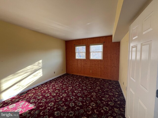 unfurnished room with baseboards, wooden walls, and carpet floors