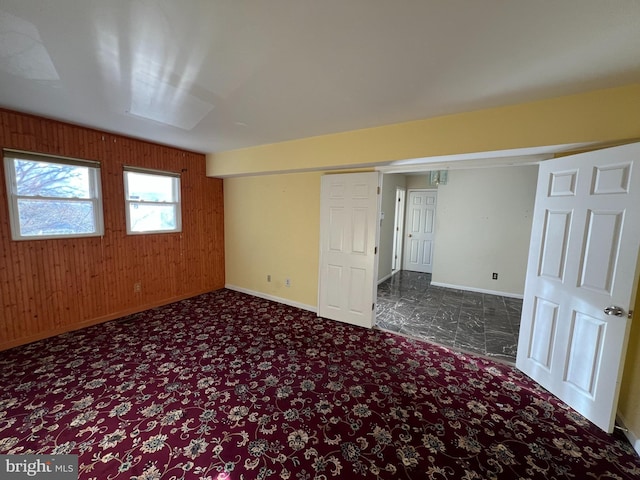 unfurnished bedroom featuring baseboards, carpet floors, and wooden walls