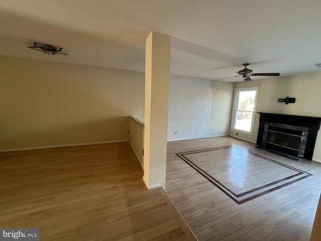 unfurnished living room with baseboards, ceiling fan, wood finished floors, and a premium fireplace