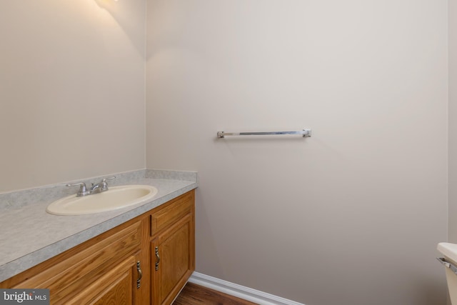 half bath with toilet, baseboards, wood finished floors, and vanity