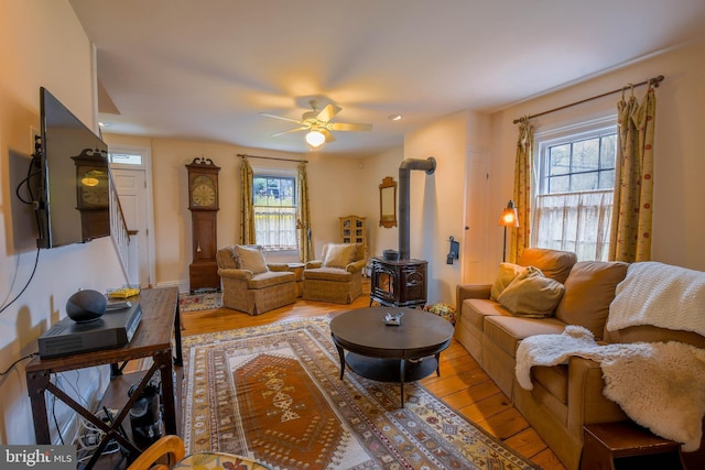 living room with a ceiling fan, wood finished floors, and a wood stove