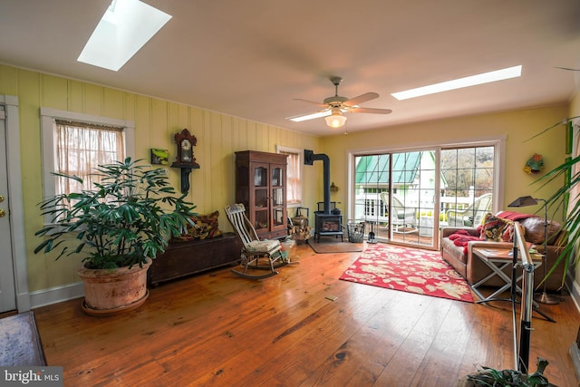 living room featuring a skylight, hardwood / wood-style flooring, a wood stove, and a ceiling fan