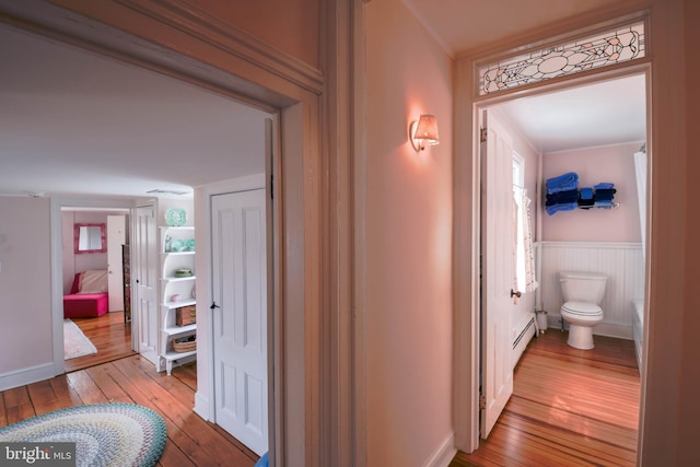 hallway with a baseboard radiator, a wainscoted wall, and hardwood / wood-style flooring