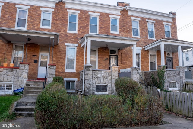townhome / multi-family property featuring cooling unit, stone siding, brick siding, and fence