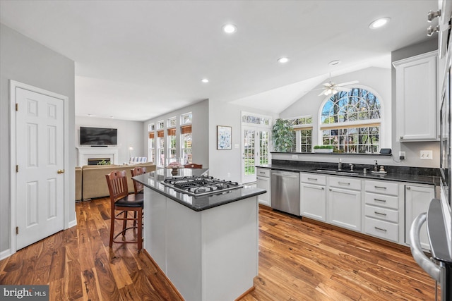 kitchen with wood finished floors, appliances with stainless steel finishes, ceiling fan, white cabinetry, and open floor plan